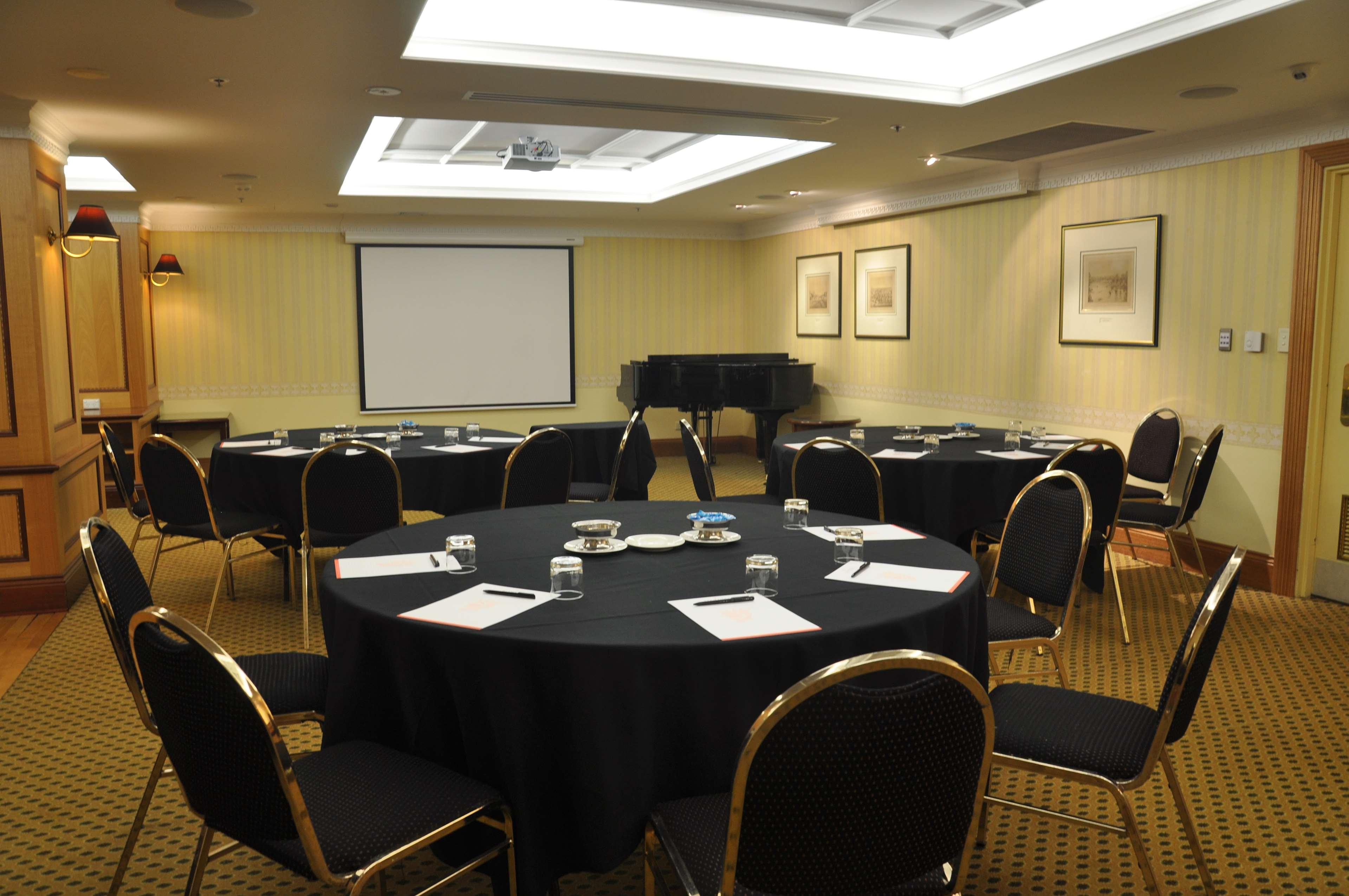 מלון Stamford Plaza אדלייד מראה חיצוני תמונה The photo shows a conference room set up for a meeting or presentation. There are several round tables covered with black tablecloths, each surrounded by black upholstered chairs. On the tables, there are notepads and glasses of water, indicating tha
