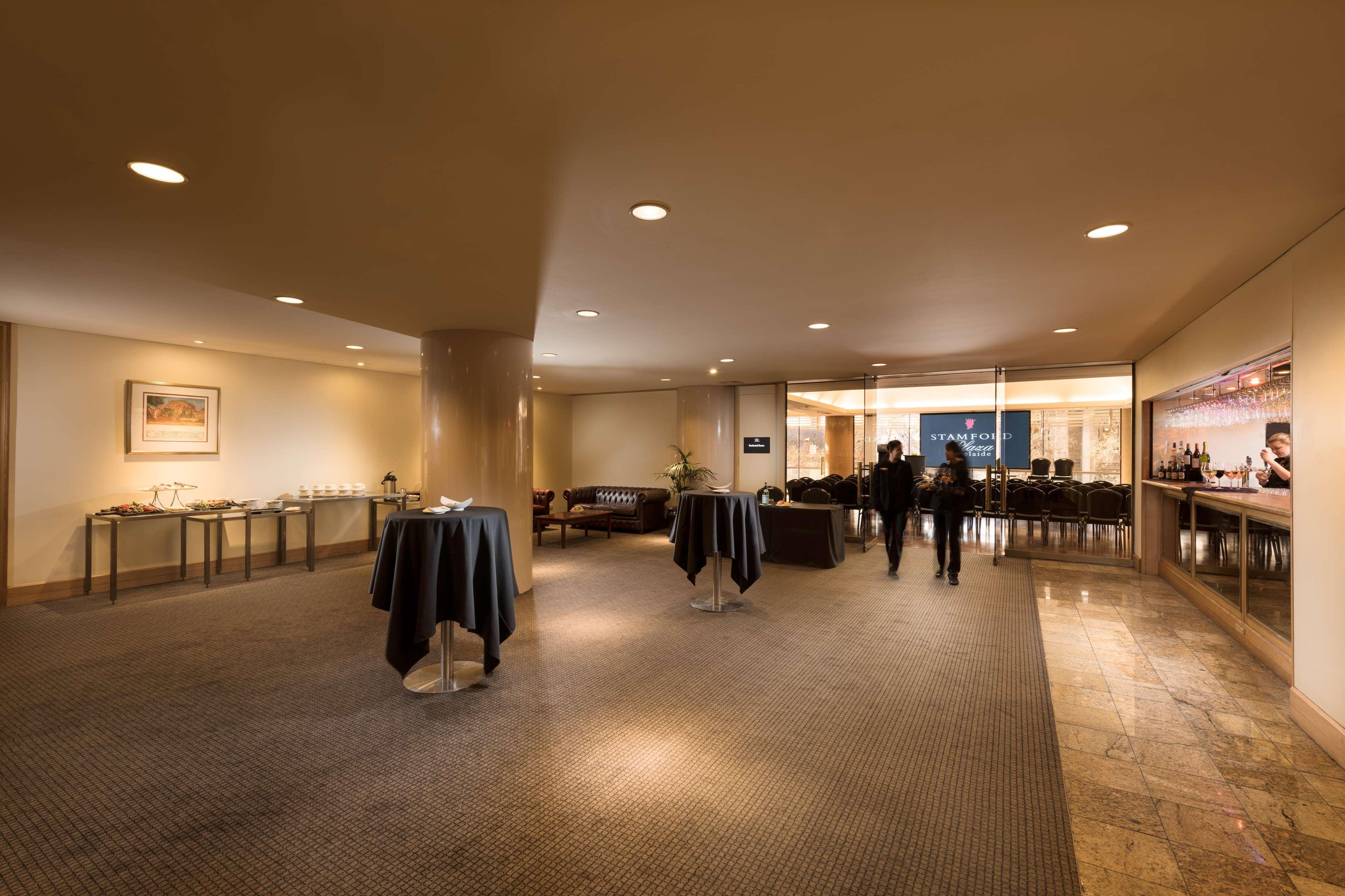 מלון Stamford Plaza אדלייד מראה חיצוני תמונה The image shows an indoor space that appears to be a lounge or reception area. There are several round tables with dark tablecloths positioned throughout the room. The floor is carpeted, and the lighting is warm and somewhat dim. In the background, t
