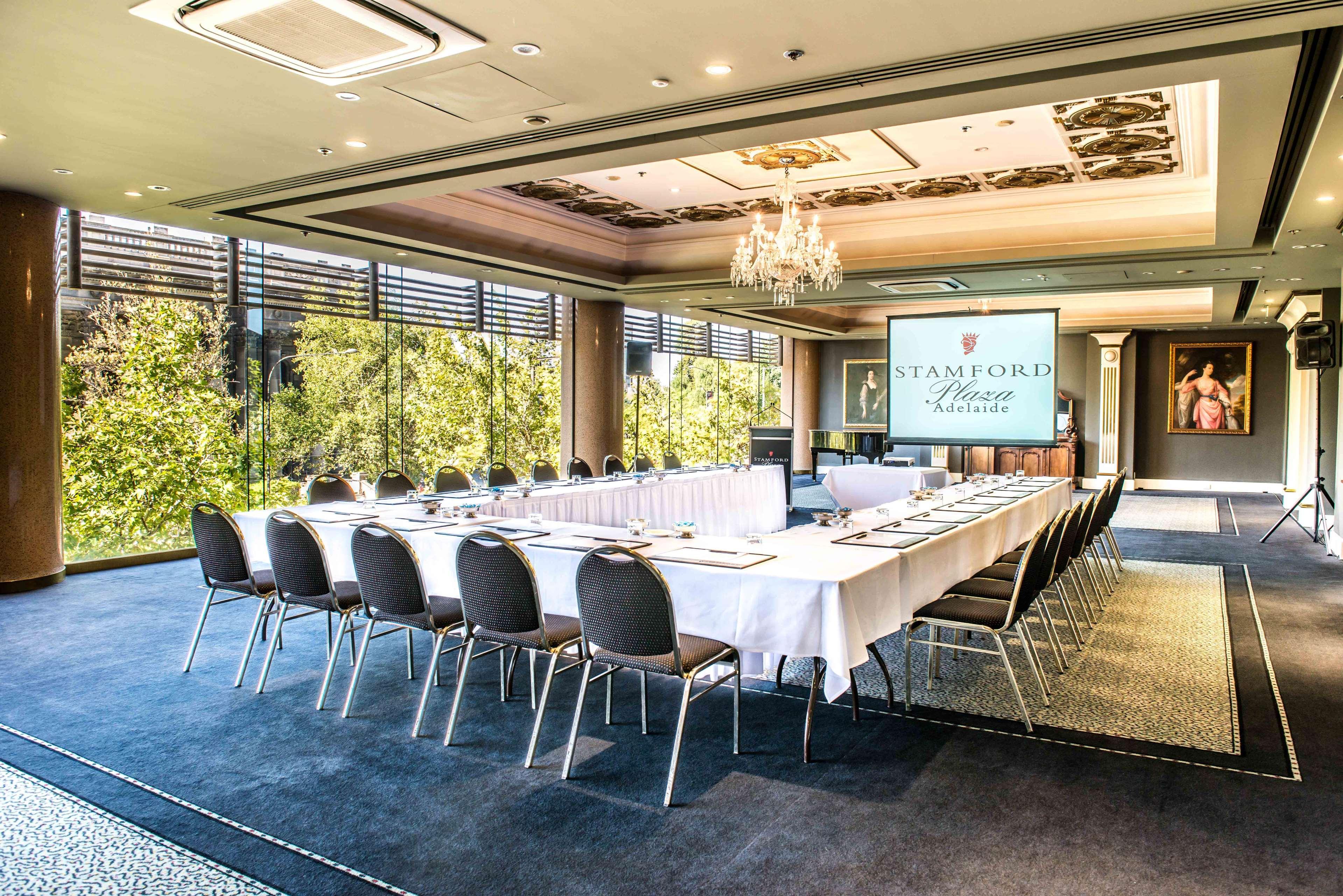 מלון Stamford Plaza אדלייד מראה חיצוני תמונה The photo shows a stylish conference room set up for a meeting or event. There is a long rectangular table covered with a white tablecloth, surrounded by black chairs. A large screen displays the name "Stamford" along with a logo. The room features l